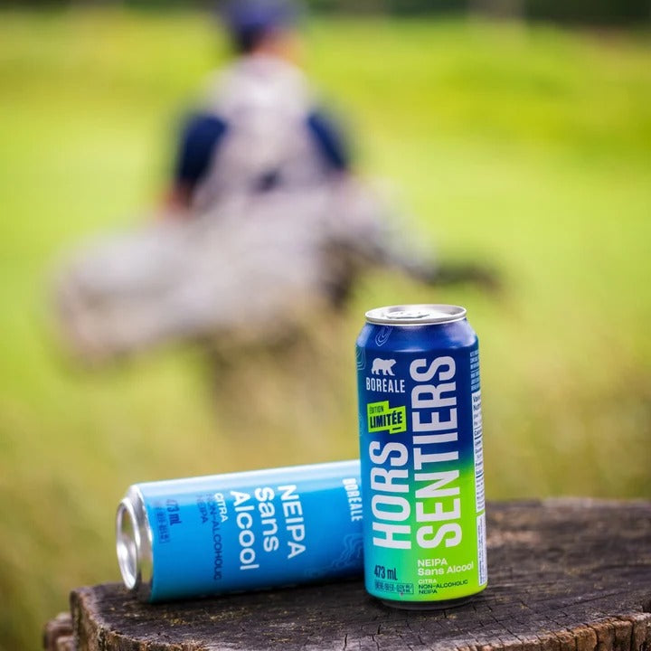 Canettes de Boréale Hors Sentiers NEIPA sans alcool sur une souche, golfeur en arrière-plan